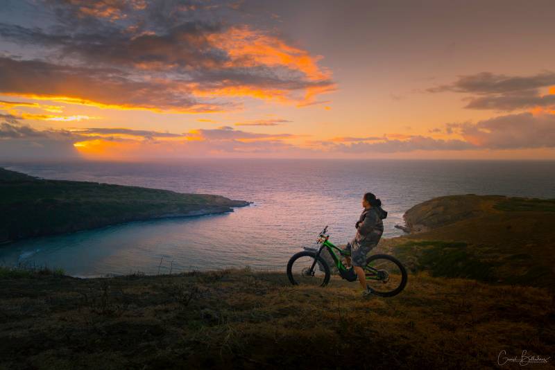 photo: bicyclist on bike overlooking an ocean bay along the shoreline. Bicycling tours in Hawaii.